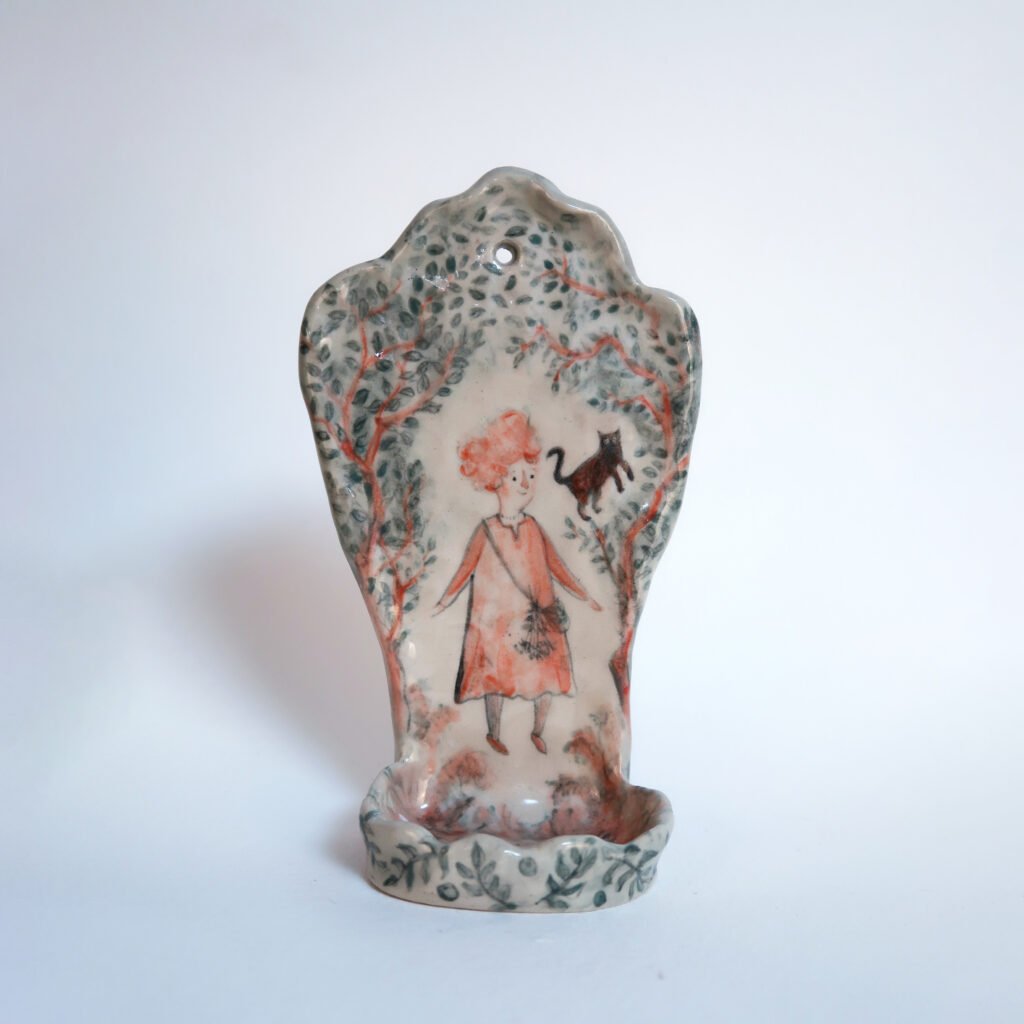 a handbuilt ceramic wall sconce for a candle with an underglaze illustration of a witchy girl and her feline companion