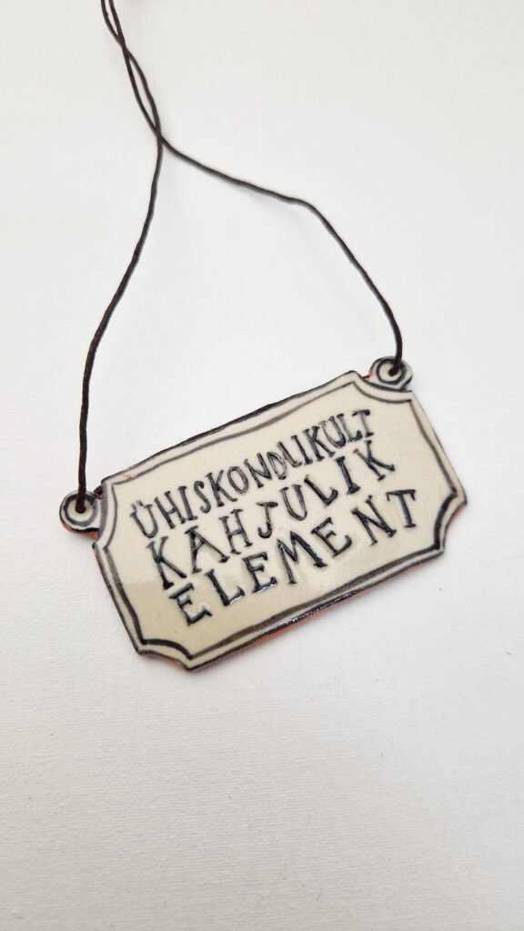 rectangular ceramic pendant with the words ühiskondlikult kahjulik element