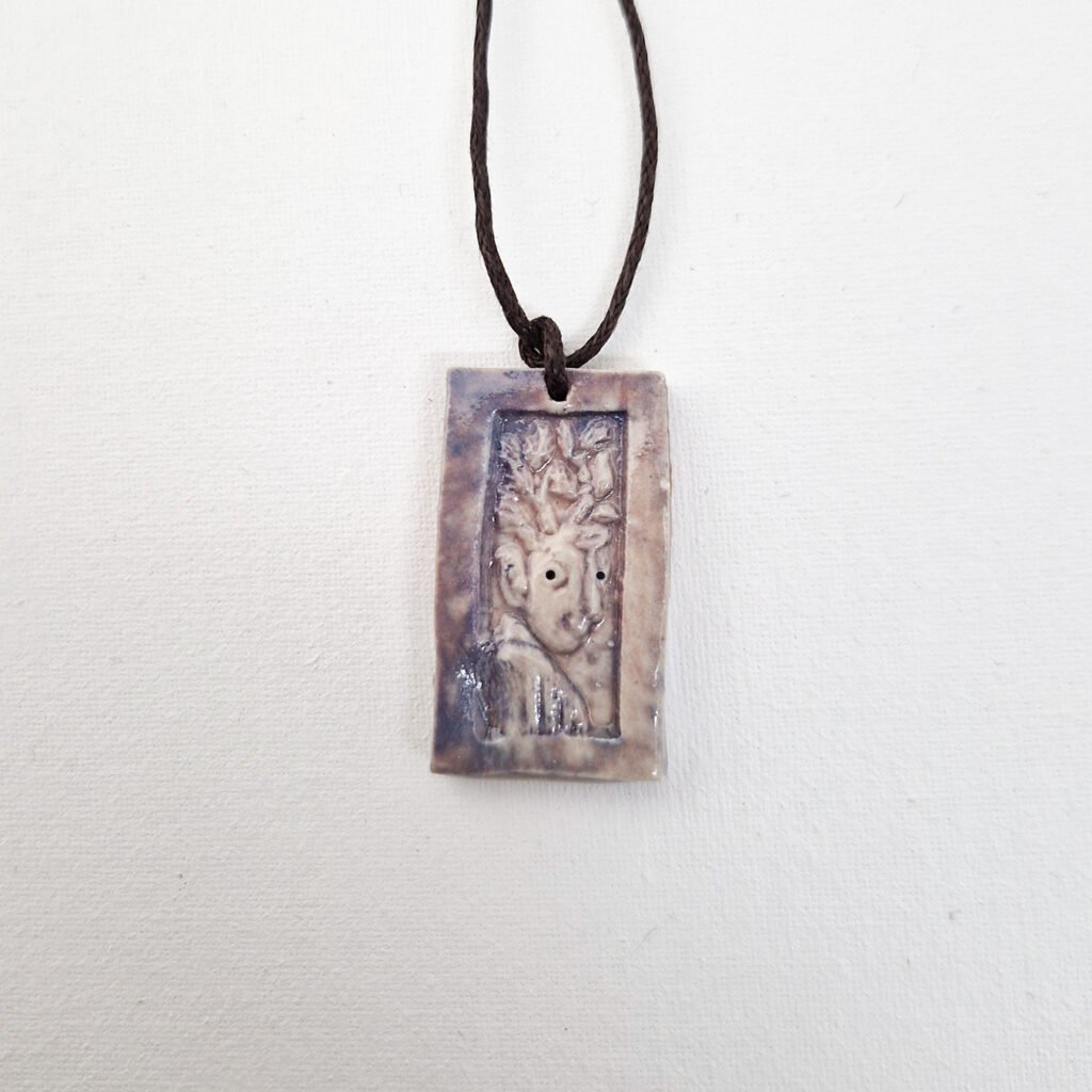 rectangular ceramic pendant depicting a creature with branches as hair