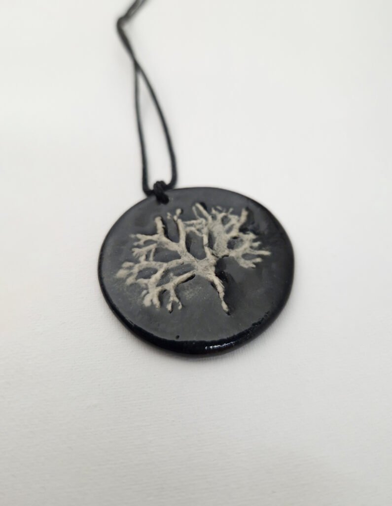 the back of a black ceramic pendant with a bar-relief of a lichen