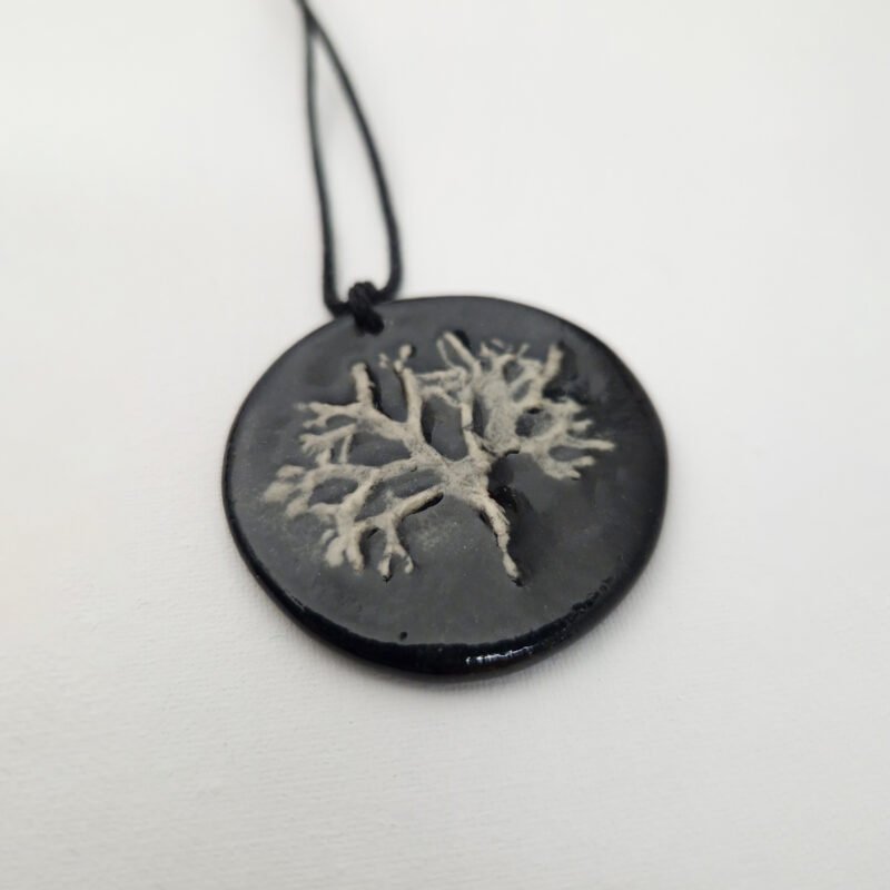 the back of a black ceramic pendant with a bar-relief of a lichen