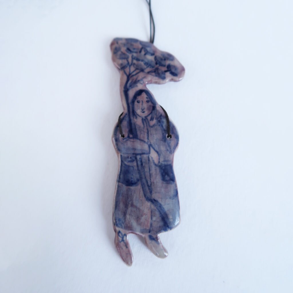 photo of ceramic pendant with an illustration of a girl holding a flower umbel