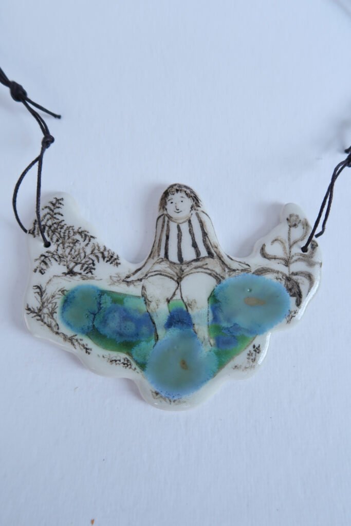 photo of a large ceramic pendant depicting a girl with her legs dipped in a small pond