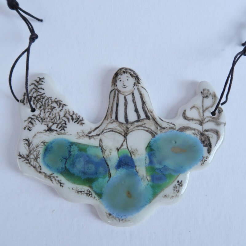 photo of a large ceramic pendant depicting a girl with her legs dipped in a small pond