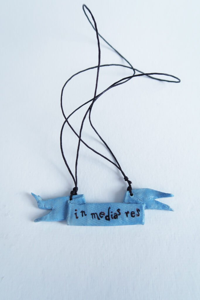 photo of a ceramic pendant in the shape of a tattered rag and with the words in medias res