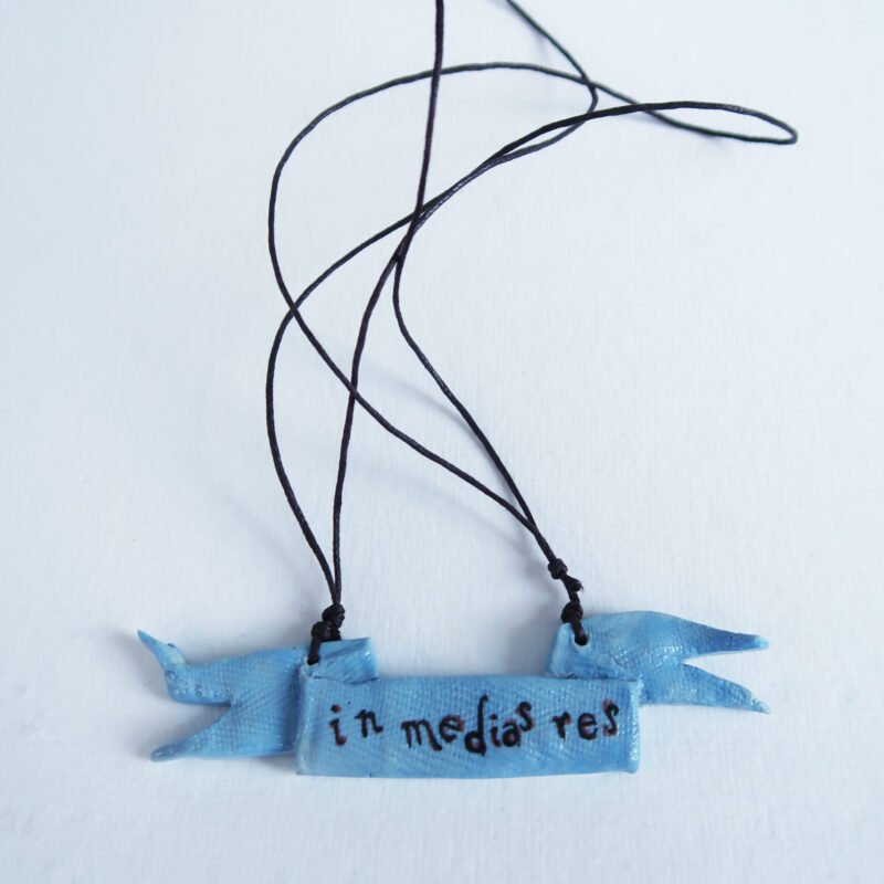 photo of a ceramic pendant in the shape of a tattered rag and with the words in medias res