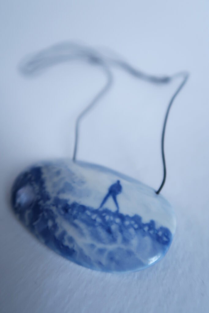 ceramic pendant with a blue underglaze painting of someone striding over a landscape