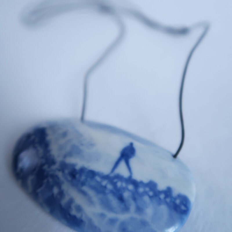 ceramic pendant with a blue underglaze painting of someone striding over a landscape