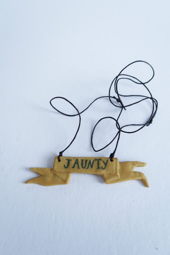 ceramic pendant in the shape of a tattered flag, with the word "jaunty"