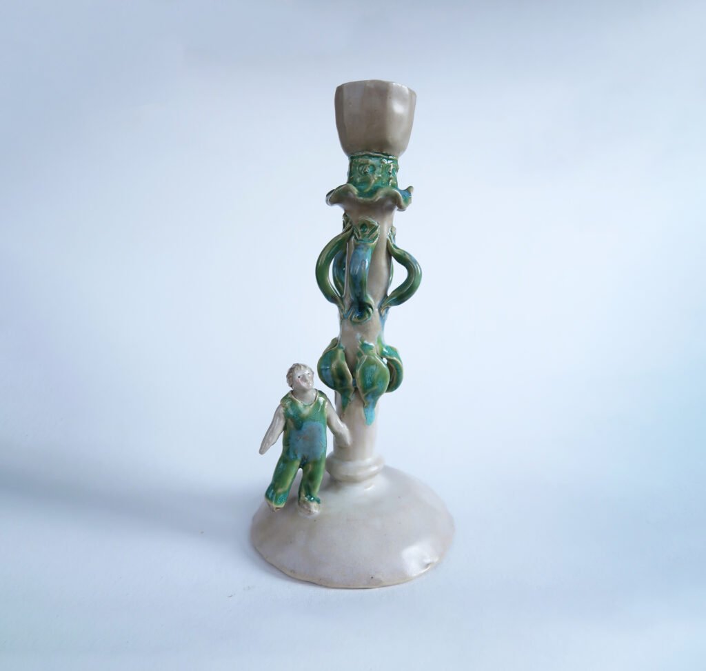 photo of a handmade ceramic candlestick wth a tiny figure wearing overalls