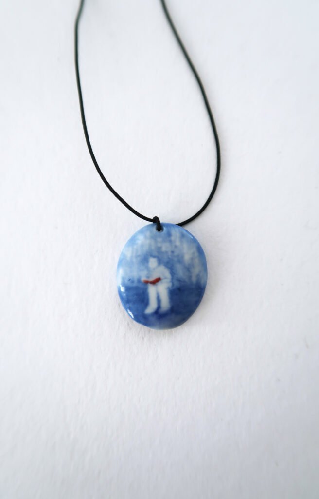ceramic pendant with a blue underglaze painting of a girl reading a book