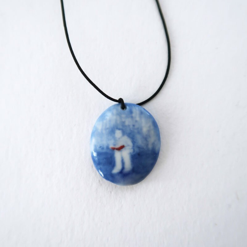 ceramic pendant with a blue underglaze painting of a girl reading a book
